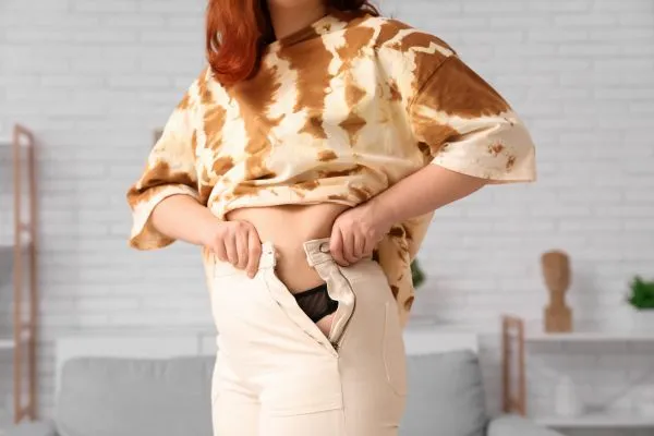 Image of woman trying to do her trousers up after pregnancy weight gain Tonbridge